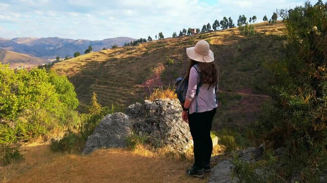 Woman traveler with peruvian hat admires scenic Cusco valleys near Rumiwasi ruins, Peru