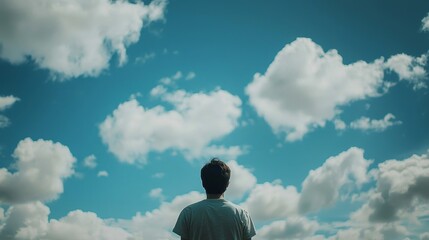 An individual stands with their head tilted up, observing a colorful sky with billowing white clouds.