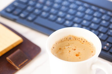 机にリング式のシステム手帳を広げ、淹れたてのコーヒー（カフェ・ラテ）を飲みながら、パソコンでデスクワークをしているイメージ
