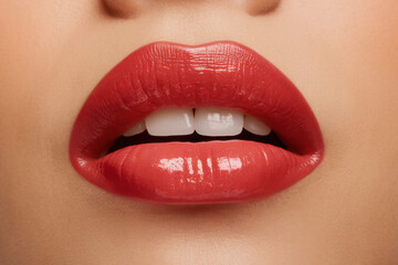 Fototapeta premium A close-up of glossy red lips slightly parted, with a hint of white teeth showing against a clean background