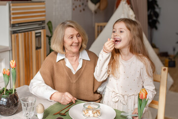 Elderly woman grandmother and little granddaughter joyfully set the table at home in the kitchen, learn etiquette