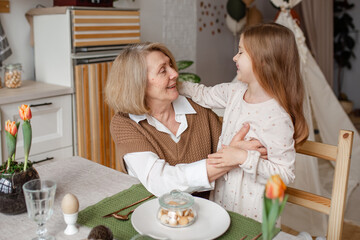 Elderly woman grandmother and little granddaughter joyfully set the table at home in the kitchen, learn etiquette