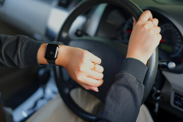 An asian young female driver checks time on watch, sits in car, stuck in traffic jam and being late for meeting with colleagues, has to delay it. Driving and in rush and has to get work in time.	