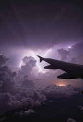 Fototapeta premium Dramatic airplane wing above thunderstorm with lightning, intense atmosphere
