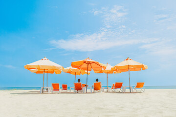Wide angle photo of couple sit on orange umbrella chair set on the beach.