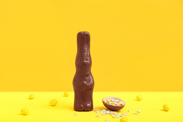 Chocolate Easter egg with sprinkles, candies and bunny on colorful background