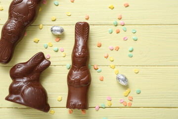 Chocolate bunnies, Easter eggs in foil and sprinkles on yellow wooden background