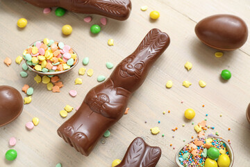 Chocolate Easter eggs with sprinkles and bunnies on beige wooden background