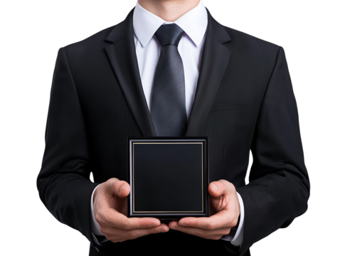 A man in a formal suit holds a small, sleek black box in both hands, presenting it with an air of anticipation. - Powered by Adobe