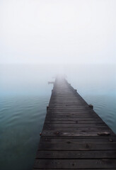 Fototapeta premium Misty pier extending into calm water at dawn, serene solitude