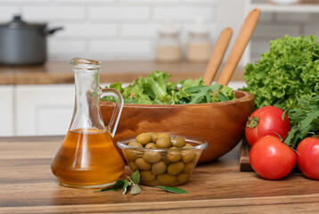 Jug with oil, olives, vegetables and fresh salad on table in kitchen