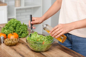 Woman adding olive oil into bowl with tasty salad at table in kitchen