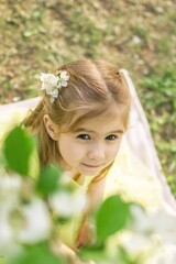 Adorable little girl with blue eyes in yellow dress joyfully playing under blossoming apple tree.