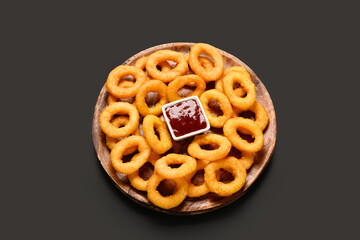 Wooden board with fried breaded onion rings and ketchup on black background