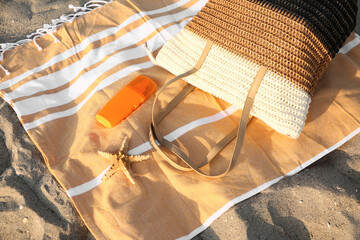 Towel with stylish beach bag, bottle of sunscreen cream and starfish  on sand, closeup