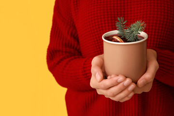 Young woman with cup of hot mulled wine on yellow background