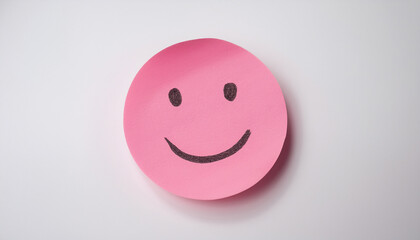 Fototapeta premium Pink sticky paper note with drawn happy emoji face on white background. Emotion, mental state