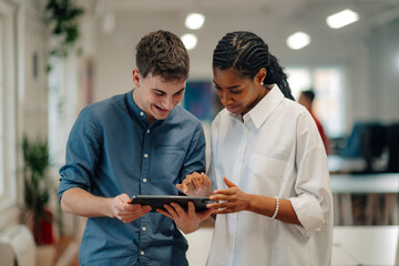 Two smiling business colleagues using digital tablet in office hallway