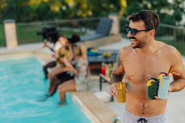 Man bringing tiki cocktails to friends at pool party
