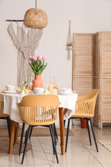 Festive table setting with vase of flowers, painted eggs and Easter bunnies in dining room