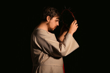 Man in Jesus robe and crown of thorns with light on black background