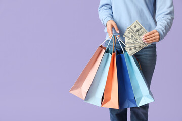 Young woman with shopping bags and money on lilac background