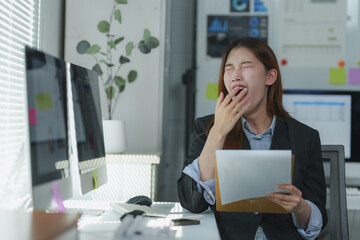 Obraz premium Tired asian businesswoman yawning while reading documents at office desk