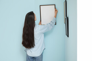 Young woman hanging picture frame on blue wall in room
