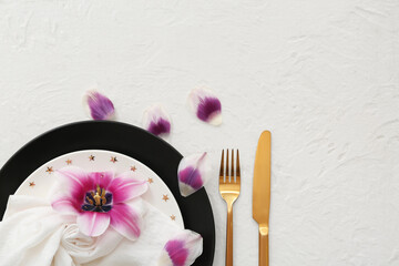 Beautiful composition with clean plates, flower, petals and cutlery on white background