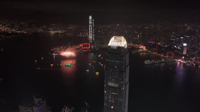 Drone shot of the IFC building at night with fireworks in the background in Hong Kong