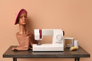 Modern sewing machine with threads and mannequin head on beige background