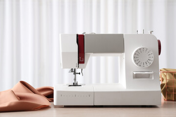Modern sewing machine with fabric and tailor's supplies on wooden table