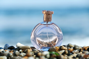 Bottle of elegant perfume on pebble beach near ocean