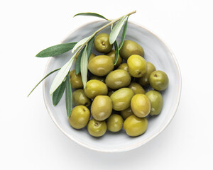Green olives with olive branch resting in a bowl on white background