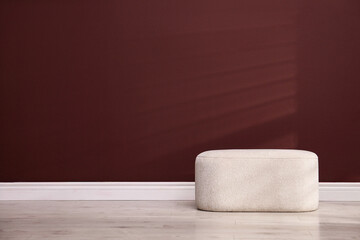 Stylish beige ottoman near brown wall indoors