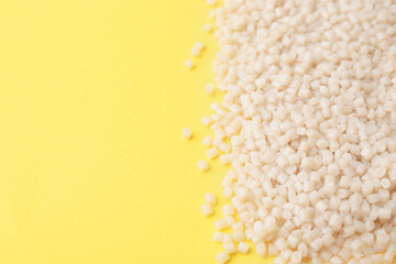 Pile of plastic granules on yellow background, closeup. Space for text