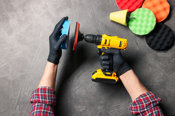 Man attaching polish pad onto electric screwdriver among colorful ones at grey textured table, top view