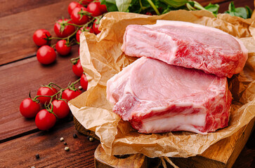 Fresh pork chops with cherry tomatoes and herbs on wooden board