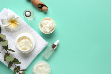 Green twig, flower, towel, bottles of cosmetic product, jars and bowl with shea butter on turquoise...