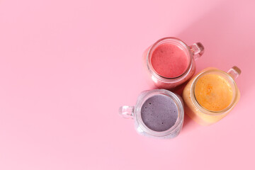 Mason jars of different fresh smoothie on pink background