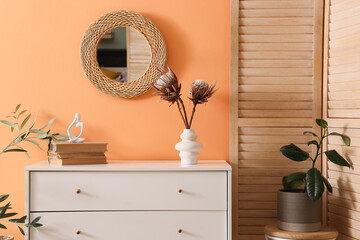 Chest of drawers with decor, houseplant, folding screen and mirror on wall