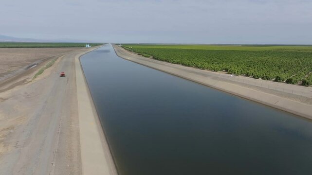 Tractor running along California aqueduct canal farmland