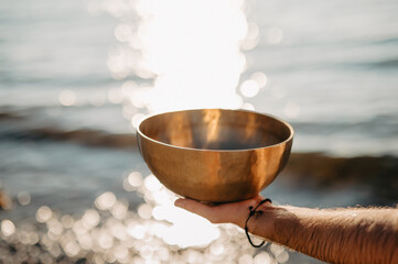 Male Hand holdng Tibetan Singing Bowl on the Beach