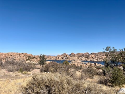 Rocky desert landscape with lake, dry vegetation under clear skies