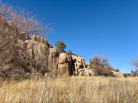 Rocky cliffs with dry grass and leafless trees under a clear blue sky