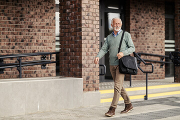 Full length of a smiling senior man walking on city street downtown.