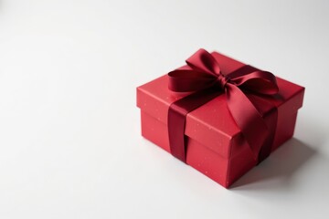A crimson gift box elegantly adorned with a rich burgundy ribbon, presenting a delightful surprise on a pristine white backdrop.