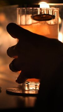 Serata romantica, la mano sul calice di un Cocktail e il calore del fuoco delle luci e del fuoco sullo sfondo.
Un Cocktail servito in una location piena di luci e di emozione.