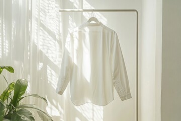 Natural light illuminates a white shirt hanging elegantly in a sunlit room with greenery