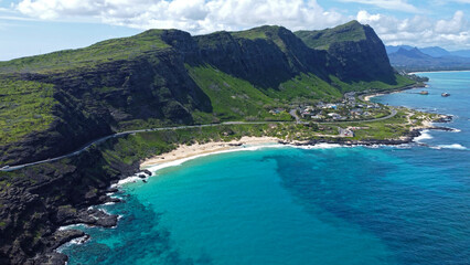 Scenic coastal road in Hawaii with turquoise ocean, sandy beach, and towering green cliffs.